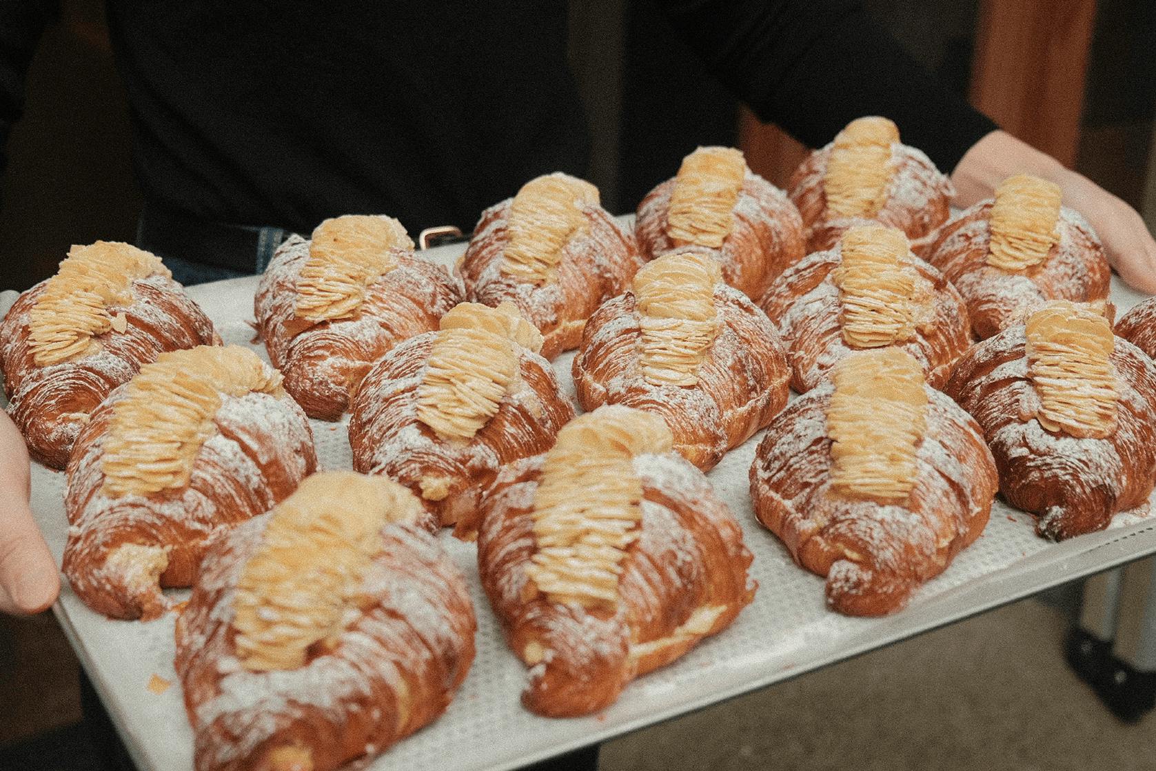 A person holding a tray of baked almond croissants.